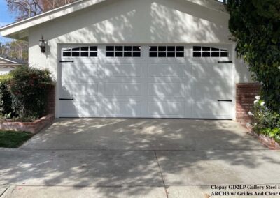 White garage featuring a modern Clopay garage door with decorative windows and hardware, set in stucco exterior.