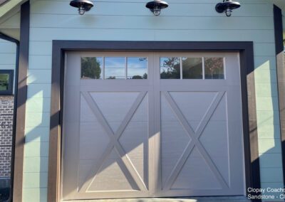 Modern farmhouse design featuring a Clopay Coachman garage door with X-pattern panels and clear glass windows.